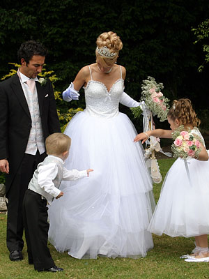 Pageboy and bridesmaid try to pick confetti out of the brides wedding dress